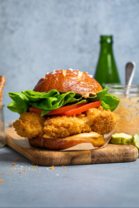 A spicy vegan cauliflower burger with fresh vegetables atop a wooden board.