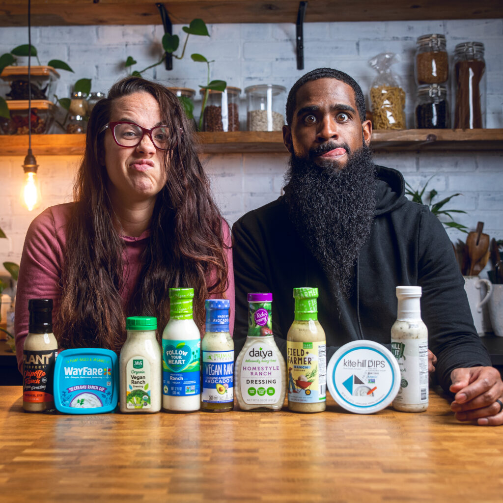 A couple posing behind a table of vegan ranch dressing products packages making funny faces