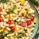 A green and brown bowl of vegan bacon ranch pasta salad topped with fresh dill.
