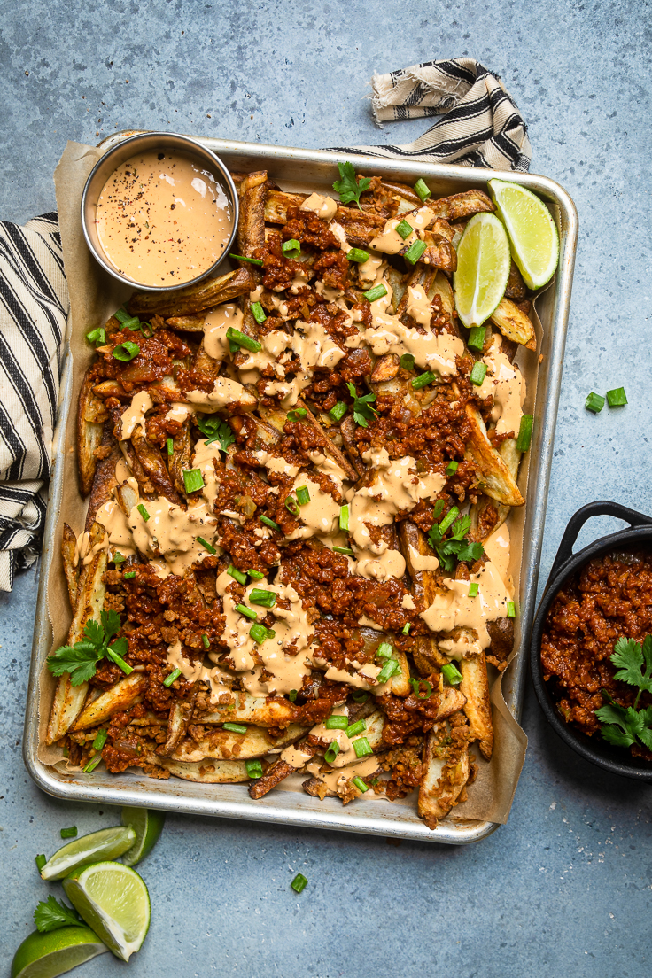Easy vegan chili cheese fries on a baking tray with more cheese sauce in bowl.