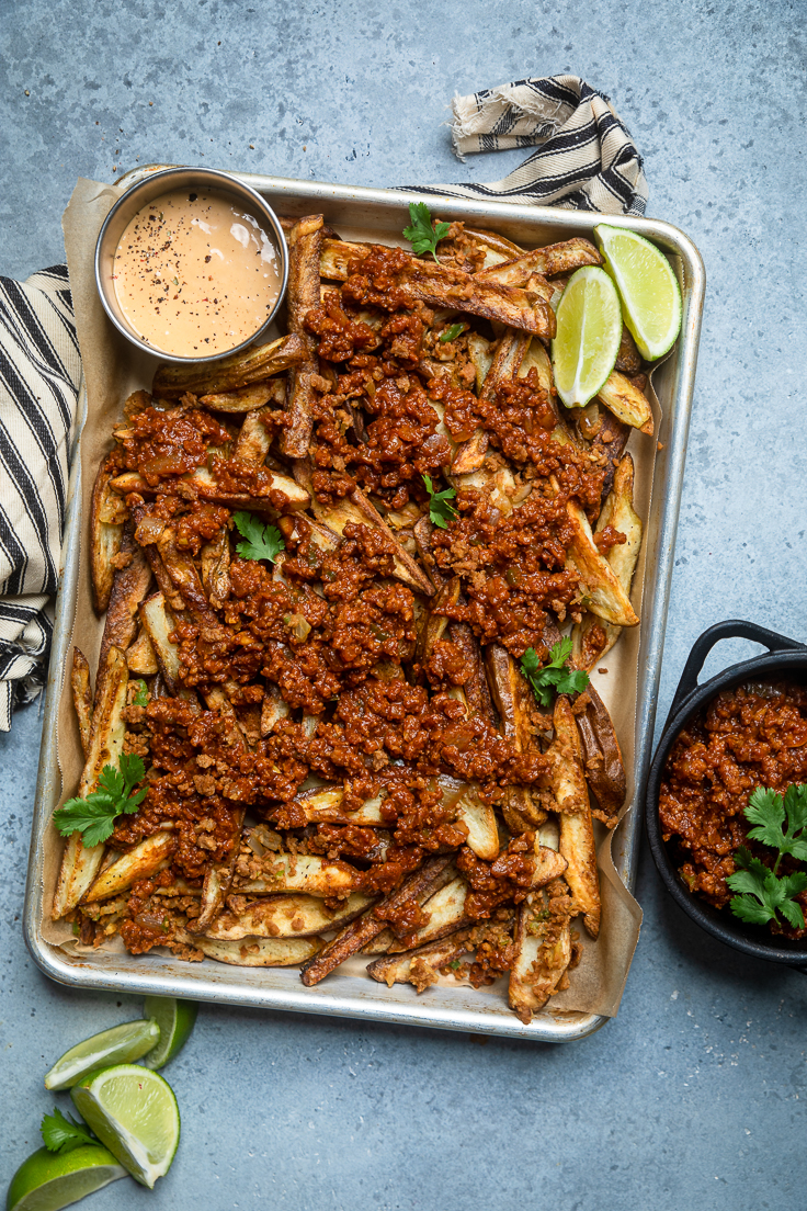 A tray of fries topped with vegan chili and a small bowl of vegan nacho cheese. 