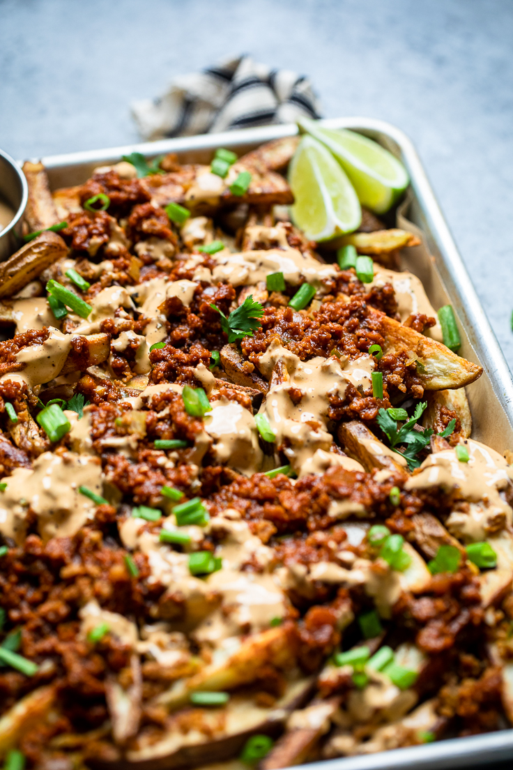 Easy vegan chili cheese fries on a tray with lime wedges.