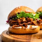 A Vegan pulled chicken sandwich atop a wooden cutting board that is round.