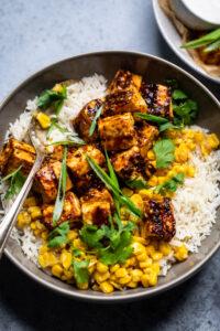 A bowl of Vegan chipotle mango BBQ tofu over rice with corn and cilantro.