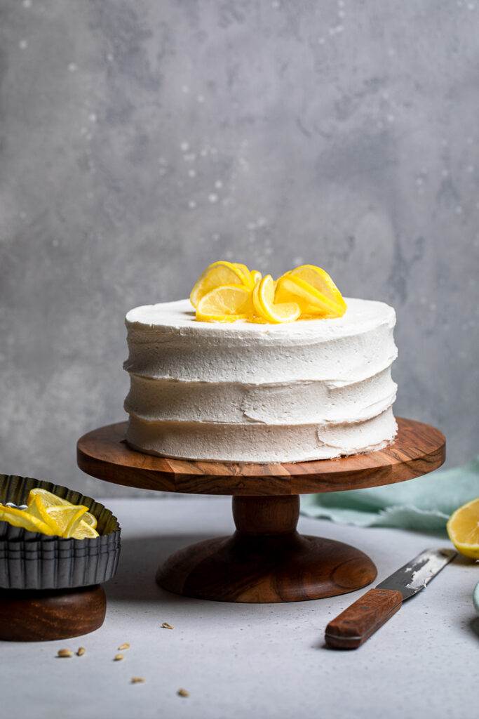 An uncut double layered Vegan Lemon Cake on top of a wooden cake stand.