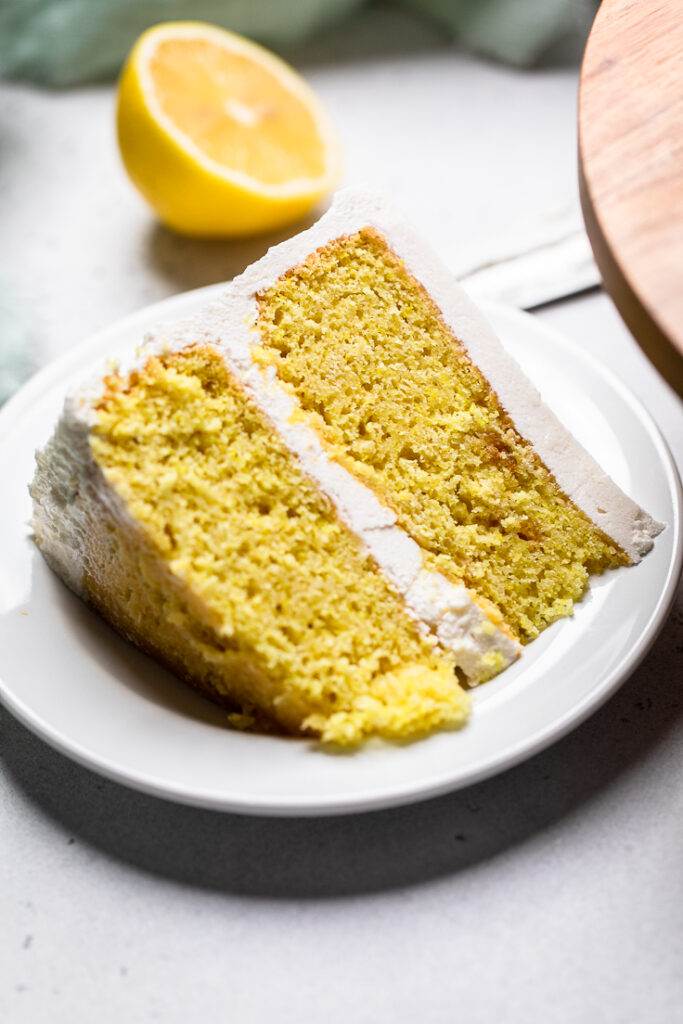 A slice of layered Vegan Lemon Cake laying flat on a white plate.