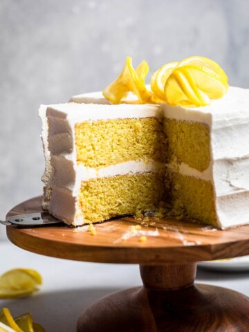 A two-layered Vegan Lemon Cake with cream cheese frosting and spiraled fresh lemons on top.