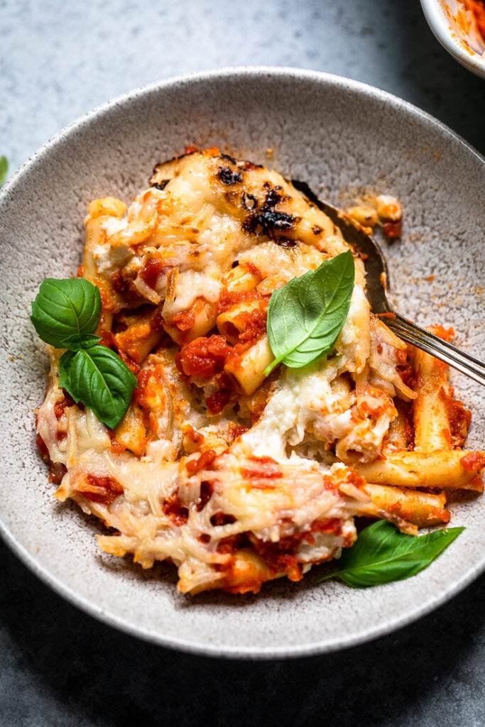 A bowl of vegan baked ziti with melted vegan cheese and fresh basil. 