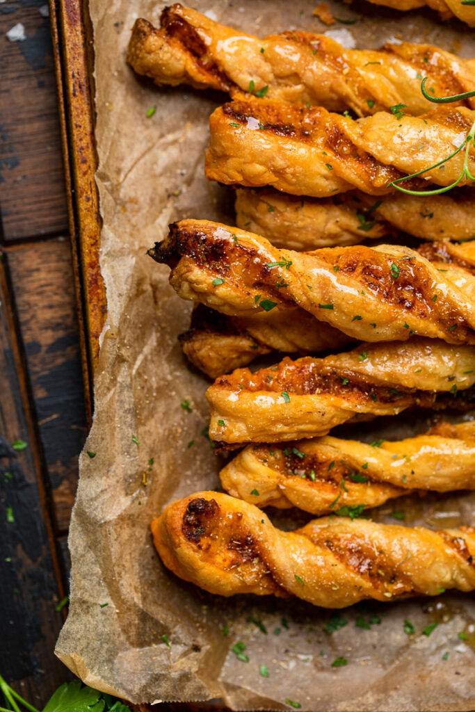 Sweet and savory vegan cheesy garlic twists on a baking sheet with parchment paper. 
