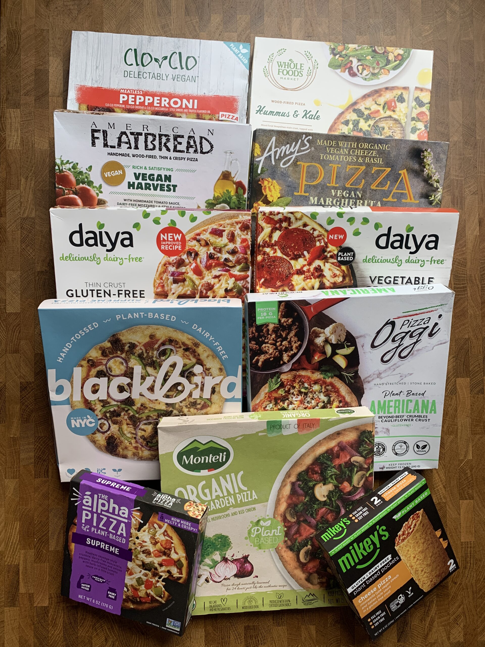 Several vegan frozen pizzas boxes on a table.