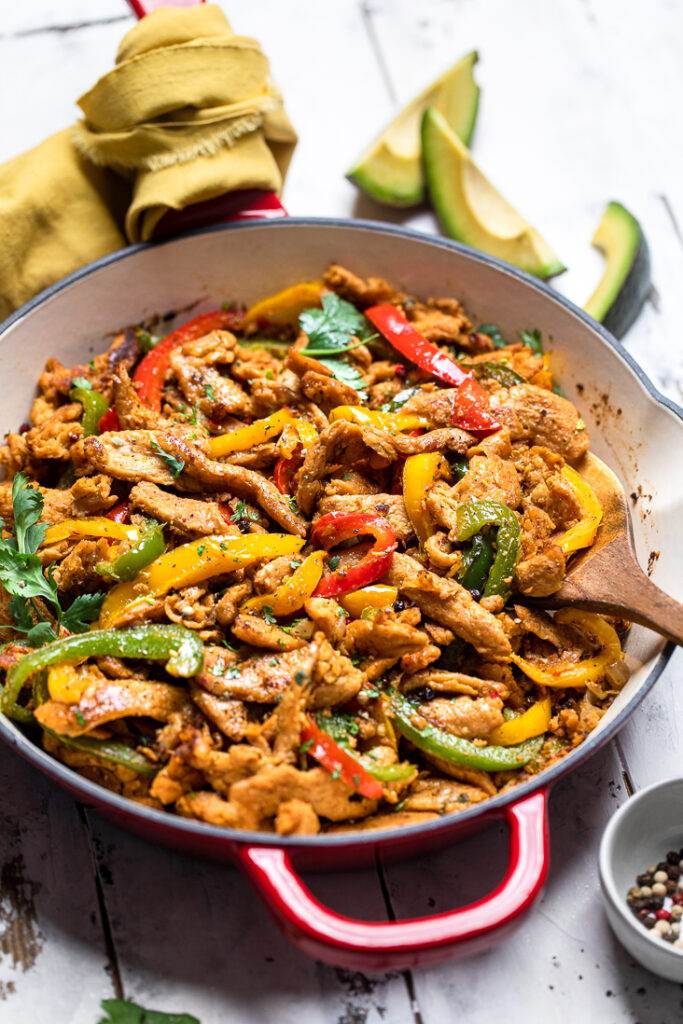 Vegan chicken fajitas made with soy curls and multicolored peppers in a white cast iron skillet. 