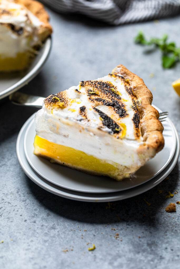 A slice of Vegan lemon meringue pie on top of two stacked plates. 