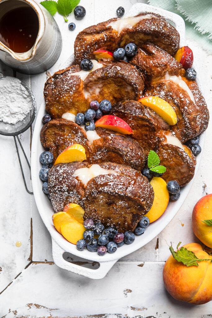 Vegan Whipped Cream Cheese Stuffed French Toast with fresh Peaches and Blueberries in a serving dish.