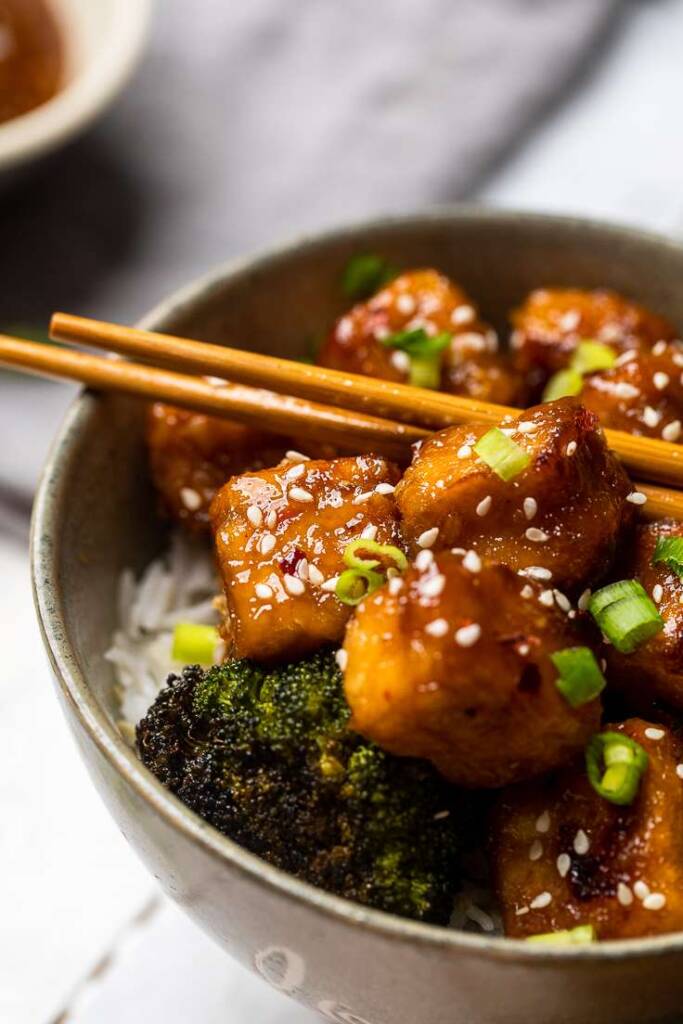 saucy Vegan General Tso\'s Tofu in a bowl with broccoli and rice. 