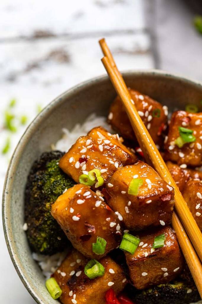 A green bowl with Vegan General Tso\'s saucy Tofu over rice with broccoli and green onions.