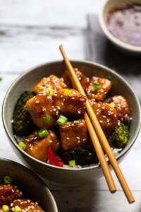 A bowl of Vegan General Tso's Tofu with broccoli and green onions.