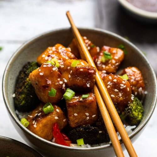 A bowl of Vegan General Tso's Tofu with broccoli and green onions.
