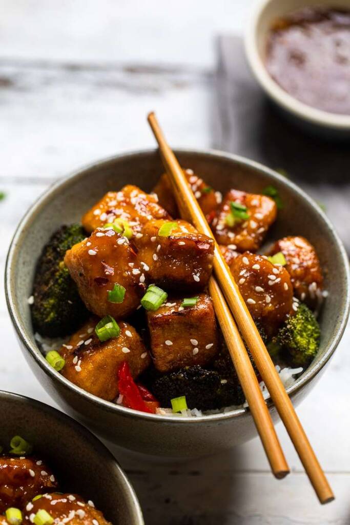 A green bowl with vegan General Tso\'s Tofu and broccoli topped with sesame seeds. 
