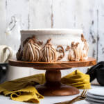 An uncut layered vegan pumpkin cake on a cake stand with pumpkins designed with frosting.