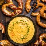 Vegan beer cheese in a small black cast iron skillet with soft pretzels surrounding it.