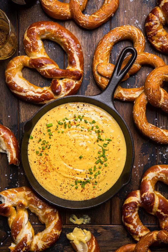 Vegan beer cheese in a small black cast iron skillet with soft pretzels surrounding it. 