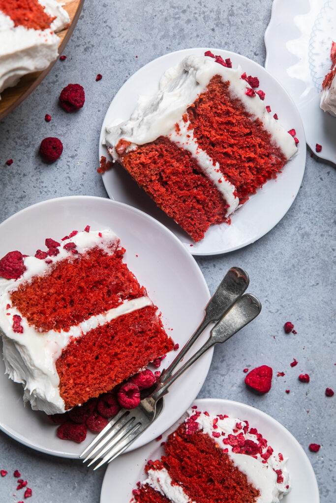 Two servings of vegan red velvet cake on white plates side by side. 
