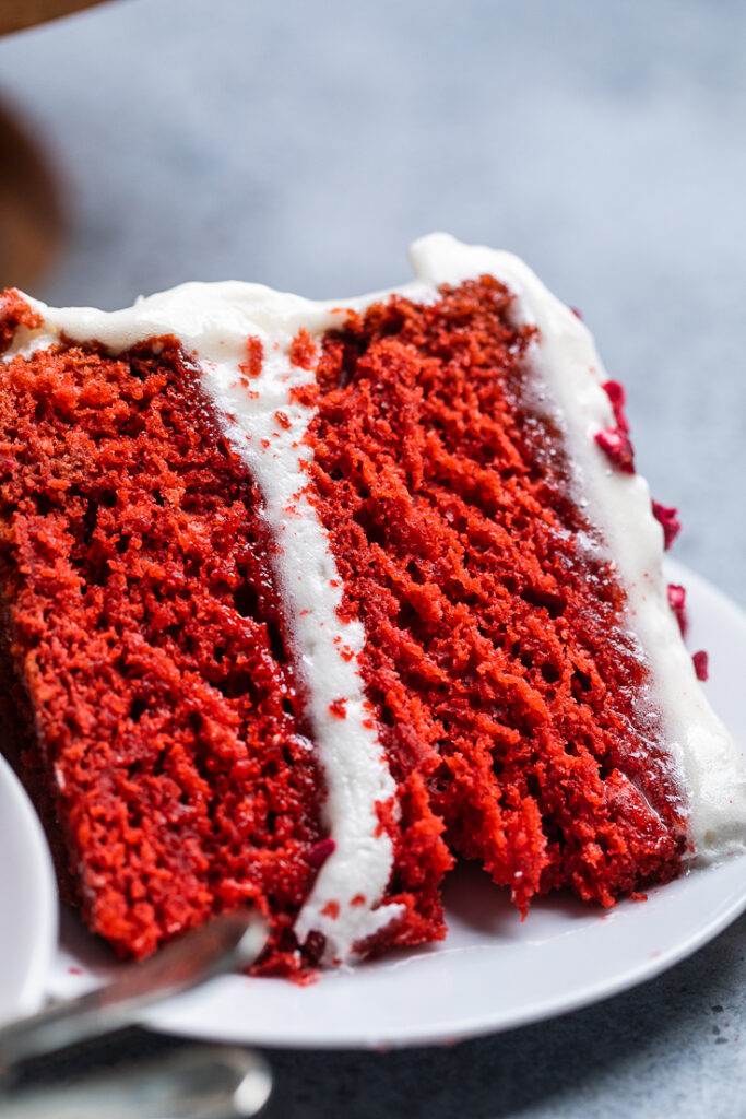 A slice of vegan red velvet cake laying flat on a plate.