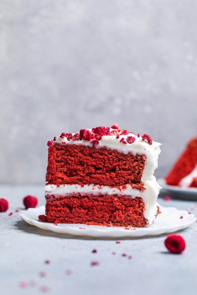 A single slice of vegan red velvet cake on a plate topped with dried raspberries.