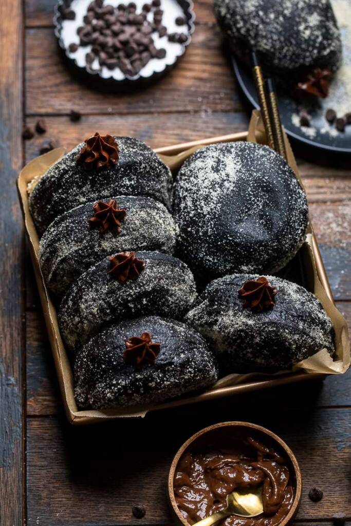 A tray full of black chocolate vegan brioche donuts on a wooden table.