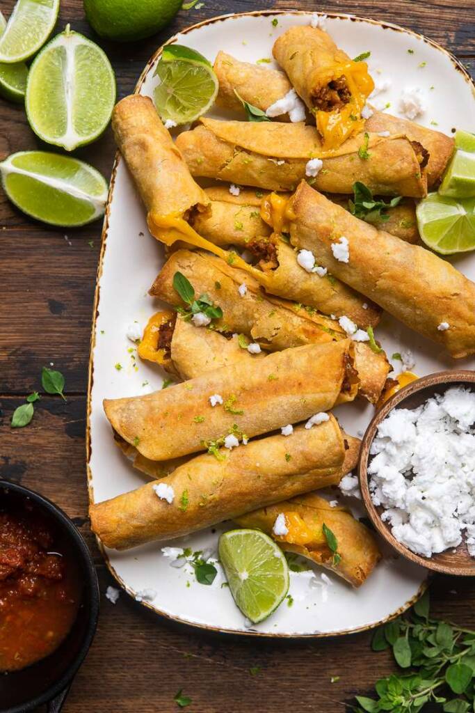 Cheesy baked vegan taquitos in a white serving dish with brown trim. 