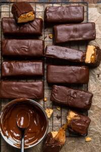 Vegan Snickers Bars lined up on a black cooling rack over brown parchment paper.