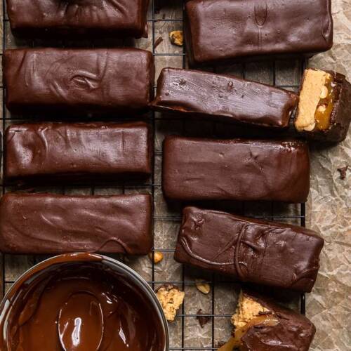 Vegan Snickers Bars lined up on a black cooling rack over brown parchment paper.