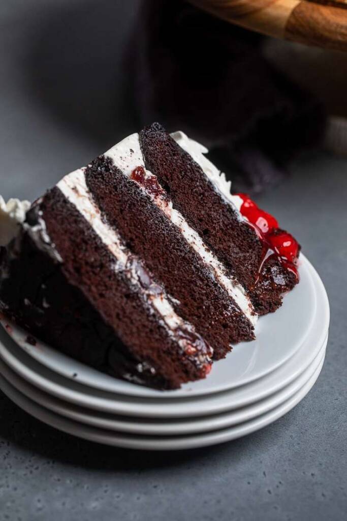 A slice of triple layered vegan black forest cake on a stack of white plates.