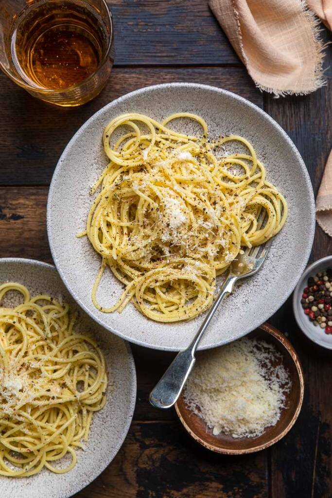 A plate of vegan cacio e pepe with vegan parmesan cheese grated on top. 