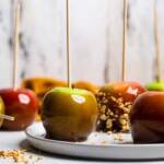 A white plate of vegan caramel apples, one with chopped peanuts on the outside.