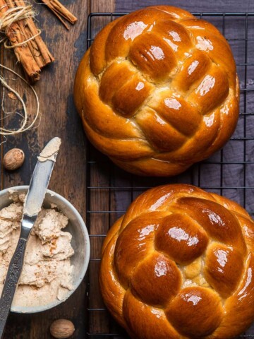 Two loaves of vegan round pumpkin challah bread with a bowl of maple cinnamon butter.