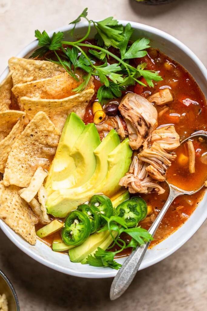 A bowl of vegan \"chicken\" tortilla soup with avocado slices and jalapeno slices.