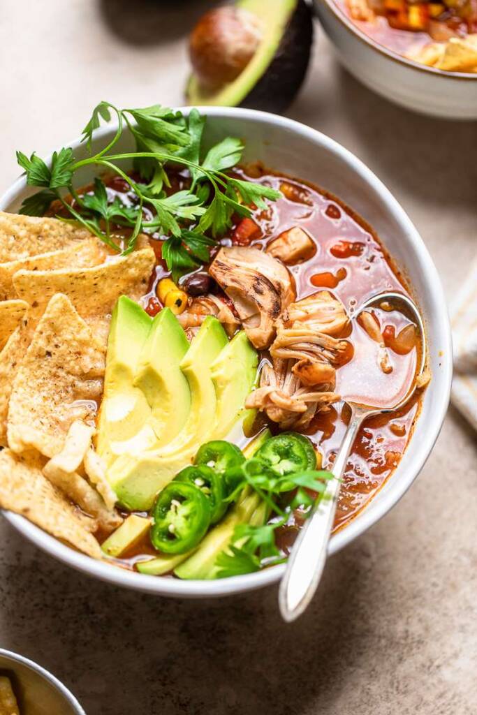 A white bowl filled with of vegan \"chicken\" tortilla soup topped with cilantro.
