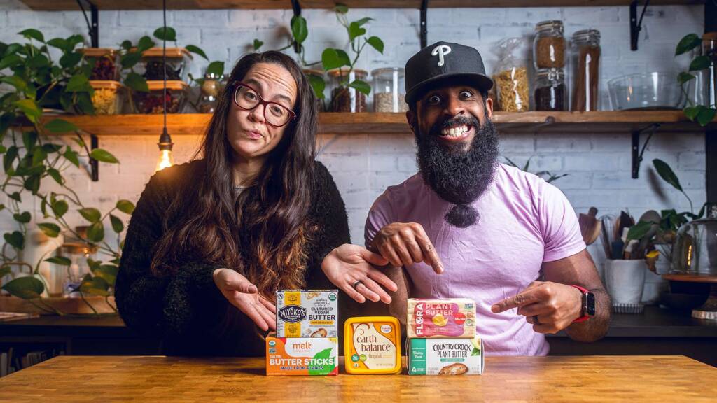 A man and a woman pointing to an assortment of vegan butters.