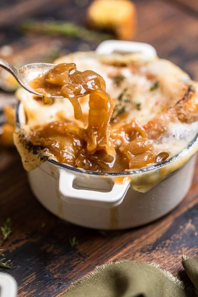 A spoonful of vegan French onion soup held over a bowl of soup.