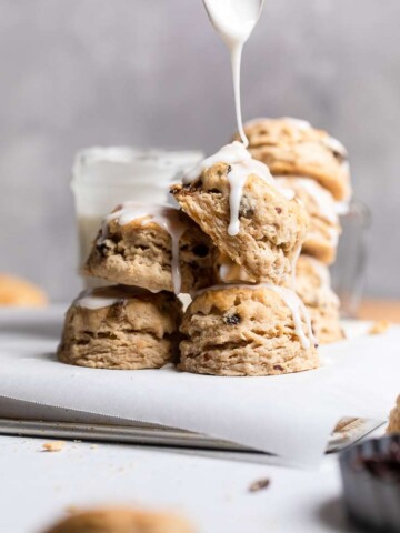A plate of stacked Vegan iced cinnamon raisin biscuits with glaze drizzling from top.