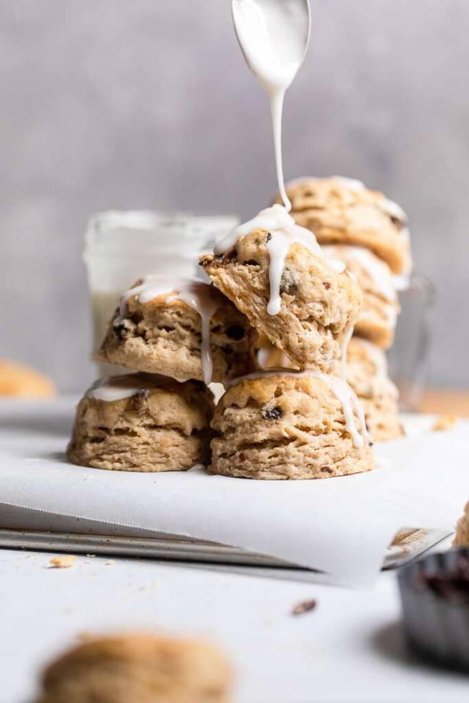 A stack of Vegan iced cinnamon raisin biscuits with a thick glaze drizzle. 