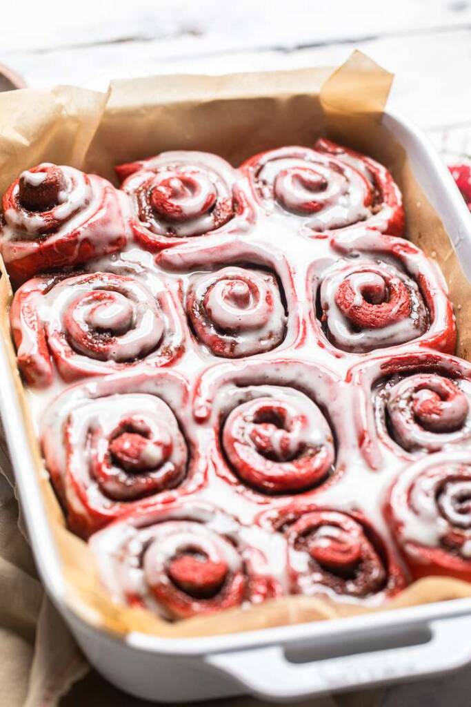 A tray of cooked and frosted vegan red velvet cinnamon rolls.