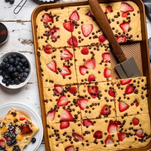 Vegan Sheet pan pancakes with strawberries and chocolate chips baked into top with spatula on side.