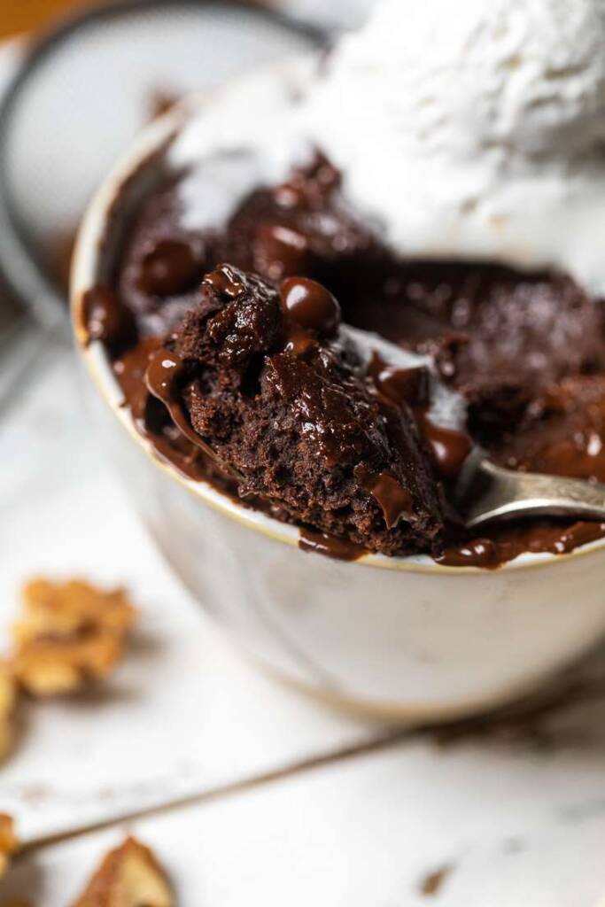 A close up of a vegan mug brownie on a spoon with melted chocolate on top. 