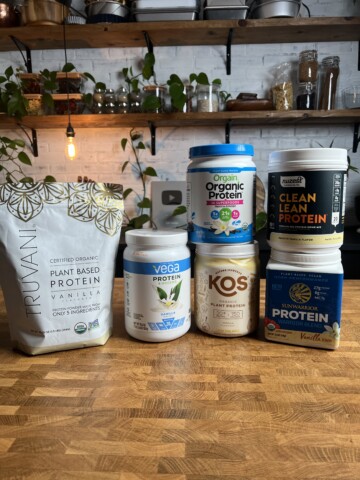 An assortment of vegan protein powders on a wood table.