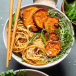 A white bowl of easy vegan sesame garlic noodles with sliced sweet potatoes and microgreens.