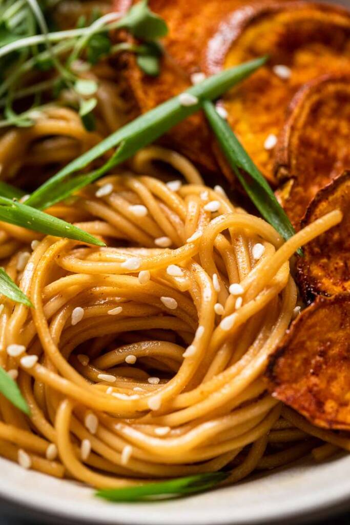 vegan sesame garlic noodles spiraled in a circle with green onions. 
