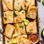 Cut Vegan sheet pan quesadillas with a bowl of salsa, lime wedges and sliced avocados.