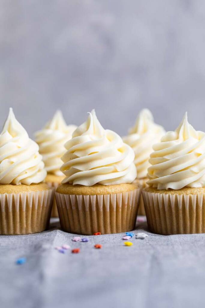 five frosted vegan vanilla cupcakes on a gray towel. 